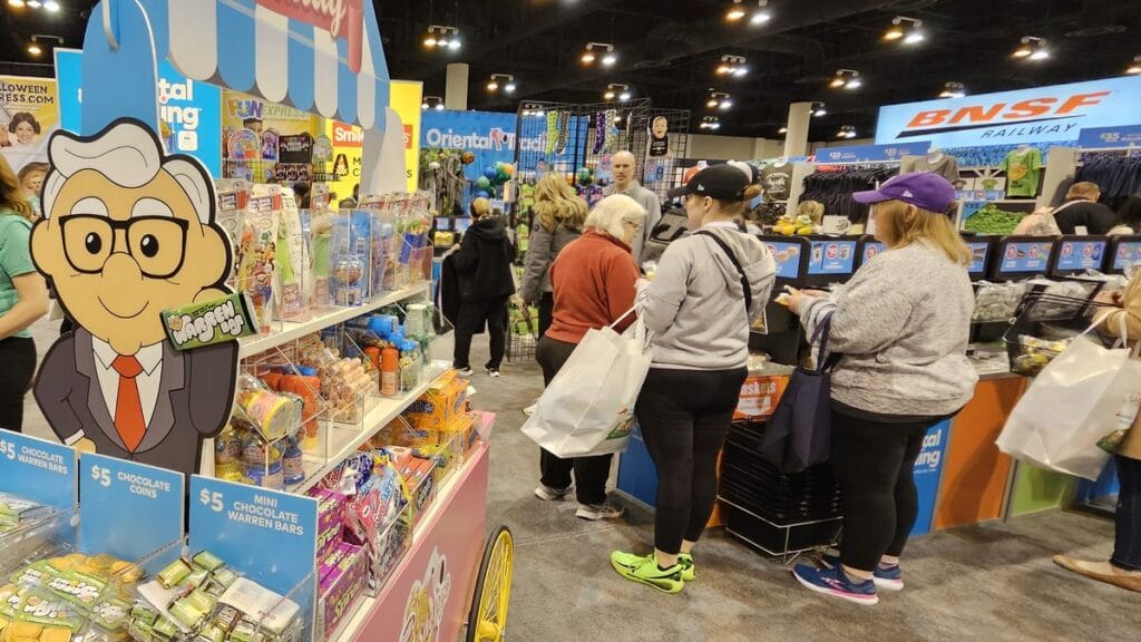 Candy cart with a Warren Buffett cartoon at the Oriental Trading booth, BNSF Railway behind, 2025 Berkshire meeting